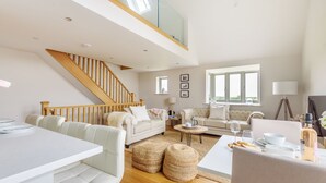 A spacious living room with a high ceiling, a wooden staircase, and a dining area with a white table and chairs. - Cobblestone Cottage - sleeps 4 guests  in 2 bedrooms (Docking)