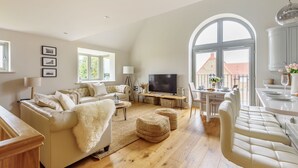 A spacious living room with a large TV, a sofa, ottomans, and a dining area with a table and chairs. - Cobblestone Cottage - sleeps 4 guests  in 2 bedrooms (Docking)