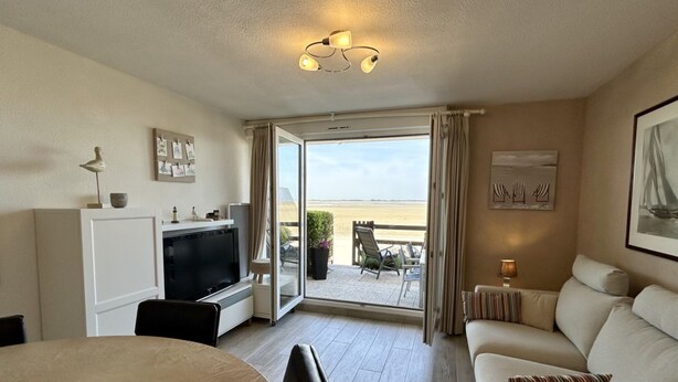 A hotel room with a TV, a sofa, a dining table, and a balcony with a view of the beach. - 🏖️ Les Pieds dans le Sable - Unique Apartment with Direct Beach Access (Le Crotoy)