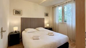 A hotel room with a bed, two bedside tables with lamps, a window with curtains, and a ceiling light fixture. - 🏖️ Les Pieds dans le Sable - Unique Apartment with Direct Beach Access (Le Crotoy)
