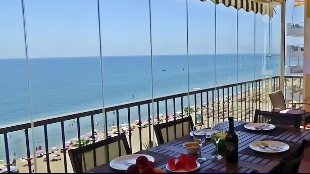 A balcony with a view of the beach and the sea. There are tables set with plates, glasses, and a bottle of wine. - Ref: 268 Stunning apartment on the beach front in Fuengirola with pool and parking (Fuengirola)