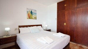 A neatly made bed with white linens and two folded towels, a wooden wardrobe, a nightstand with a lamp, and a painting of a beach scene on the wall. - Ref: 268 Stunning apartment on the beach front in Fuengirola with pool and parking (Fuengirola)