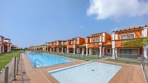 A swimming pool area with a tiled deck, adjacent to a row of orange buildings with balconies. - Holiday Home 'Orange Lux Tavira Residence 3I' with Shared Pool, Wi-Fi and Air Conditioning (Luz de Tavira)
