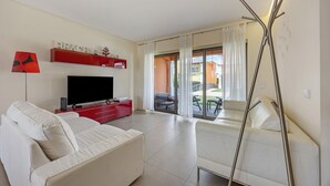 A modern living room with a flat-screen TV, a red entertainment unit, a white sofa, and a glass door leading to an outdoor area. - Holiday Home 'Orange Lux Tavira Residence 3I' with Shared Pool, Wi-Fi and Air Conditioning (Luz de Tavira)