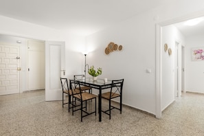 Un coin repas comprenant une table en verre, quatre chaises, une plante en pot et des éléments de décoration murale.