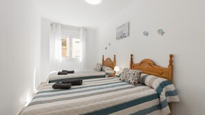Una habitación con dos camas, una ventana con cortinas, un reloj de pared y una lámpara en el techo.