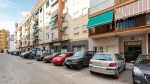 Una hilera de coches aparcados en un aparcamiento junto a un edificio de varios pisos con balcones.