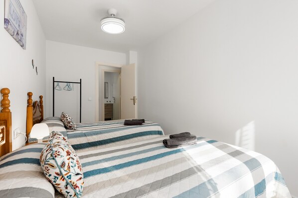Un dormitorio con una cama, cabecera de madera, mesita de noche, lámpara de pared y una puerta que da a otra habitación.