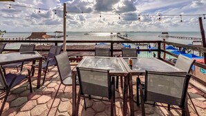 Un espace extérieur aménagé avec des tables et des chaises, offrant une vue sur une plage et une jetée.