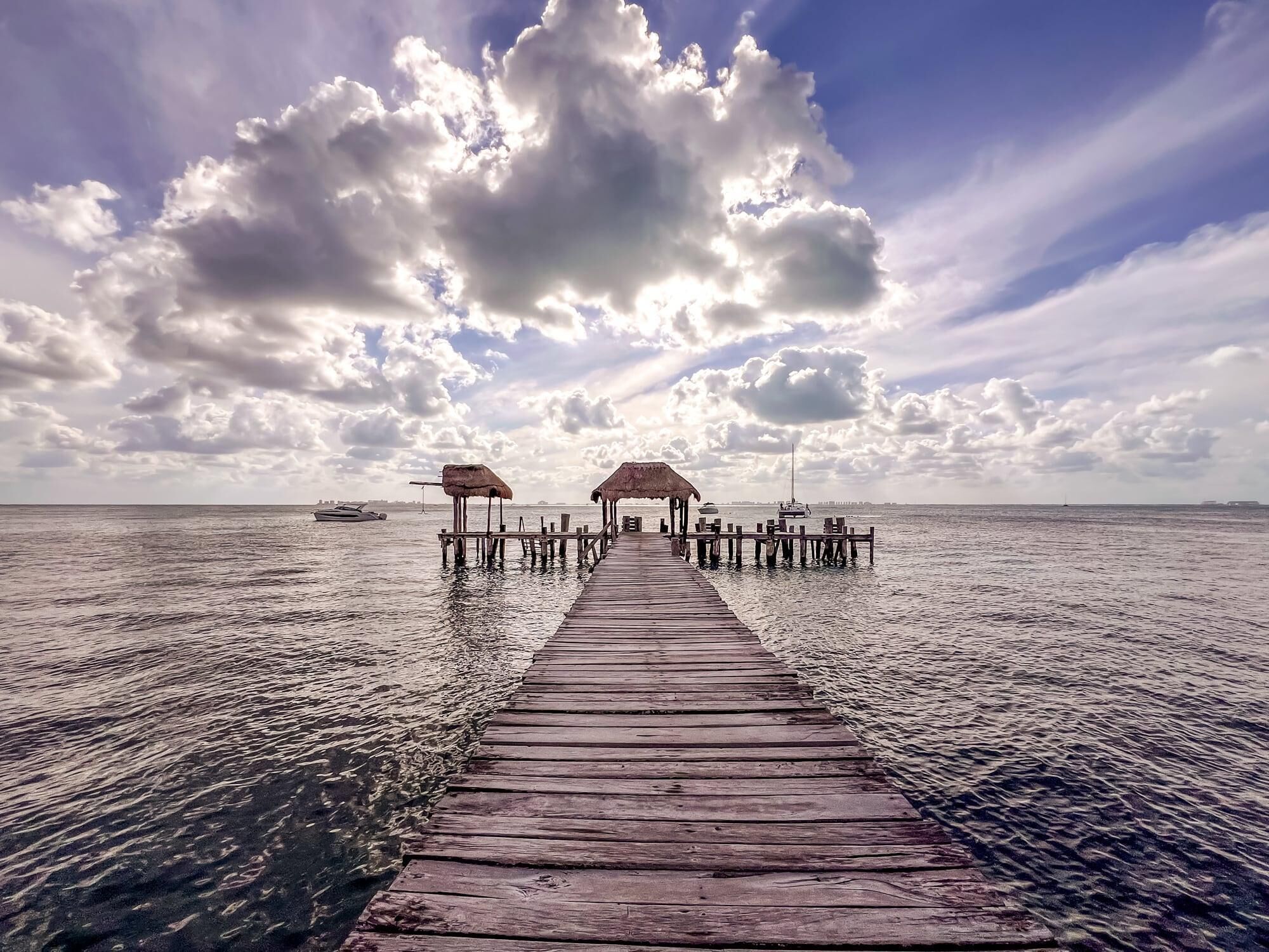 A wooden pier extending into calm waters, with thatched-roof structures at the end.