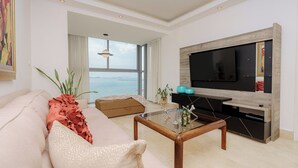 Ein modernes Wohnzimmer mit großem Fernseher, einer Couch, einem Couchtisch und Blick aufs Meer.