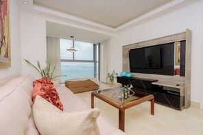 Un soggiorno moderno con una grande TV, un divano, un tavolino da caffè e vista mare.
