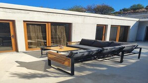 A modern outdoor seating area with a sofa and table, large sliding glass doors, and a concrete floor.