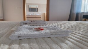 A neatly made bed with folded white towels and a small red item on the bed.