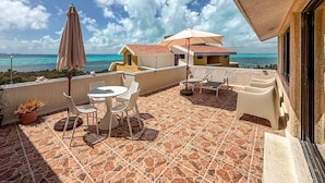 A terrace with a table and chairs, a potted plant, and a view of the sea. - Ocean View PH in Punta Sur (Isla Mujeres)