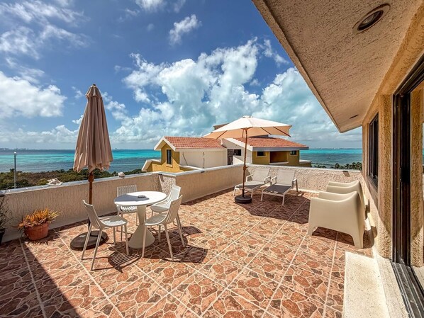 A terrace with a table and chairs, a potted plant, and a view of the sea. - Ocean View PH in Punta Sur (Isla Mujeres)