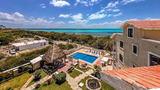 A resort with a swimming pool, a thatched-roof structure, and a view of the ocean. - Ocean View PH in Punta Sur (Isla Mujeres)