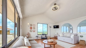 A spacious living room with a large window, a ceiling fan, a flat-screen TV, and a white sofa. - Ocean View PH in Punta Sur (Isla Mujeres)