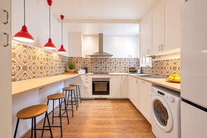 A modern kitchen with a washing machine, bar stools, and pendant lights. - Sweett | Sepulveda 5C (Barcelona)