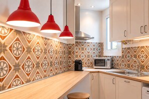 A modern kitchen with patterned backsplash, wooden countertop, stainless steel appliances, and red pendant lights. - Sweett | Sepulveda 5C (Barcelona)