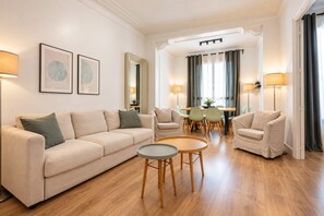 A modern living room with a sofa, two armchairs, a coffee table, and a dining area with chairs and a table. - Sweett | Sepulveda 5C (Barcelona)