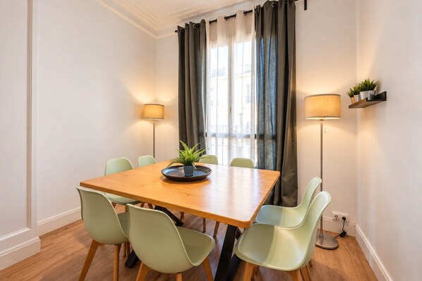 Un coin repas avec une table en bois, six chaises, deux lampadaires et une fenêtre avec des rideaux.