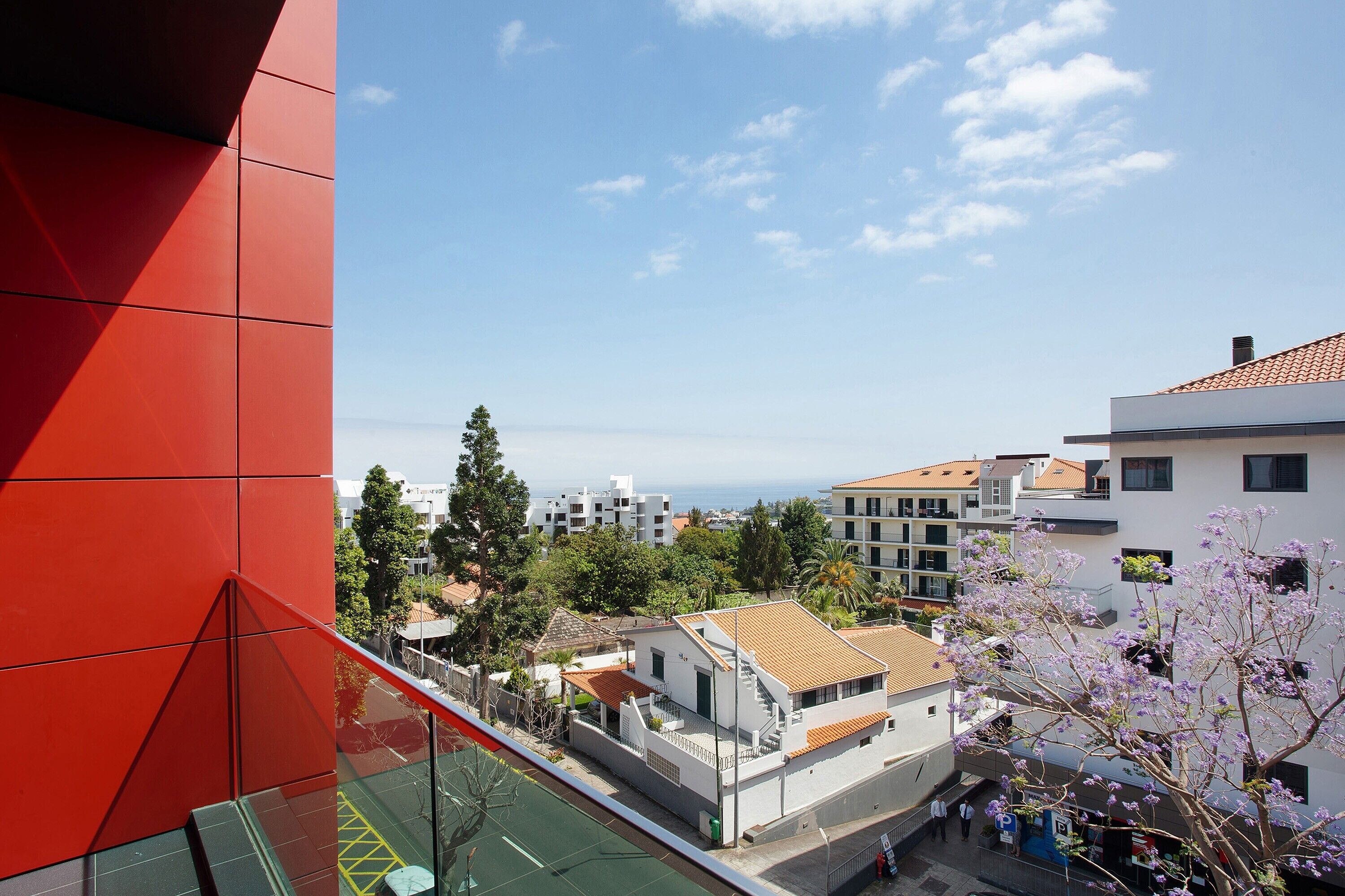 A building with a red facade, a tennis court, and a view of other buildings and trees.