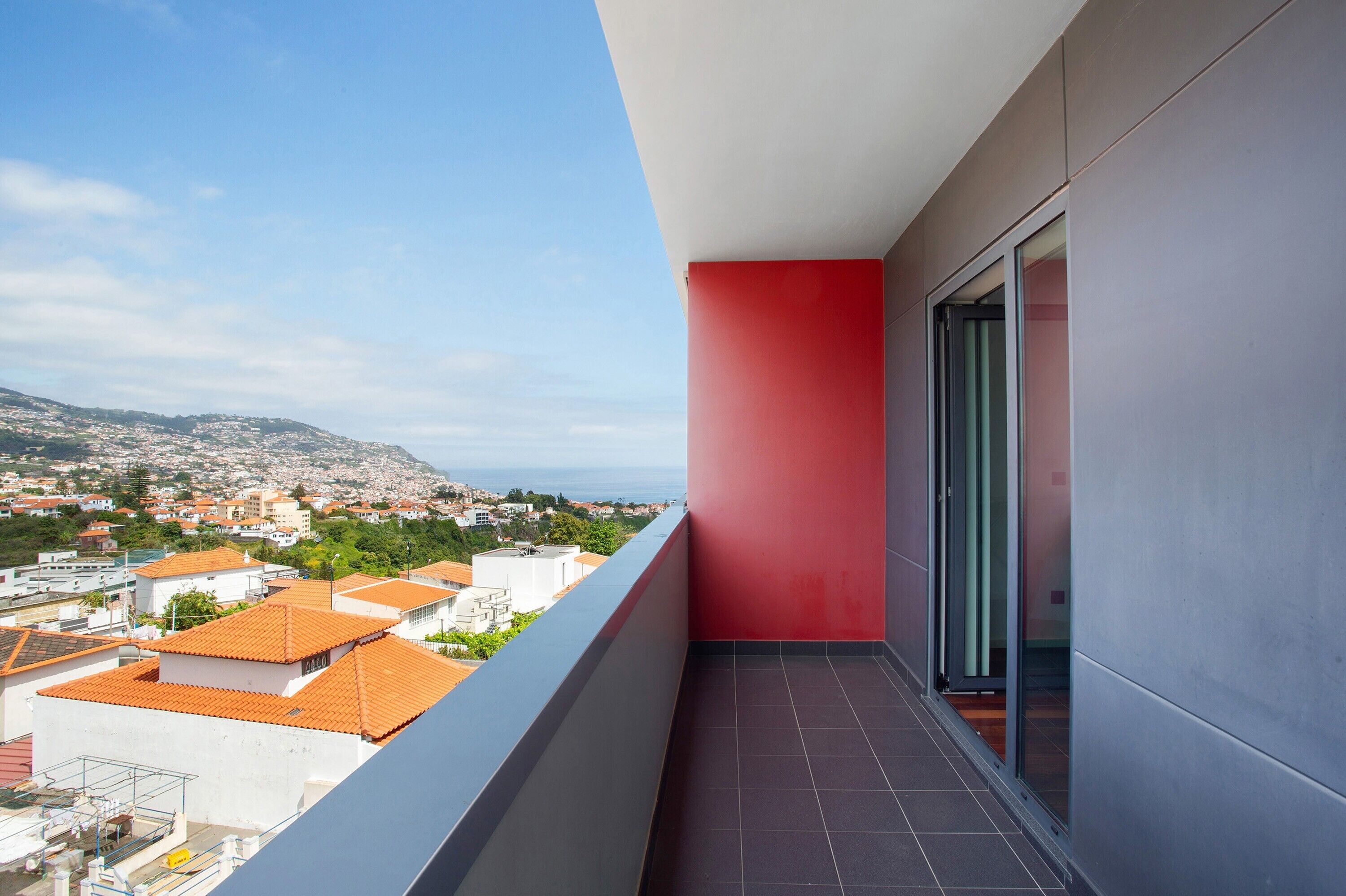 A balcony with a red wall, a glass door, and a view of a cityscape.
