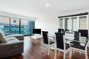 A modern living room with a sofa, dining table, chairs, a TV, and large windows. - Apartment 'Macedo' with Sea View, Balcony and Wi-Fi (funchal)