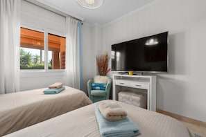 Una habitación de hotel con dos camas, televisión y ventana con cortinas.