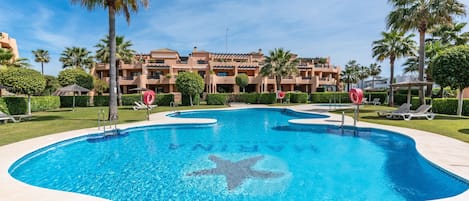 A swimming pool with a starfish design, surrounded by palm trees and a building with balconies.