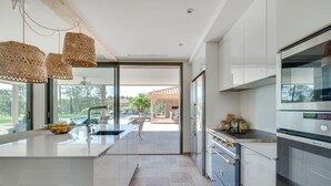 Een moderne keuken met een groot eiland, roestvrijstalen apparatuur en uitzicht op een terras met buitenmeubels.