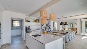 Een moderne keuken met een centraal eiland, hanglampen en uitzicht op de eethoek.