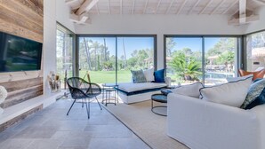 Een moderne woonkamer met een grote televisie, comfortabele zithoek en uitzicht op een zwembad en tuin.