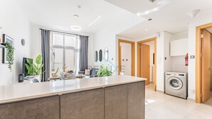 A modern kitchen with a central island, a built-in washing machine, and a large window with curtains. - Balcony Offering Community Views 1BR w/AsstRm,Walking Distance to CommunityPark (Dubai)