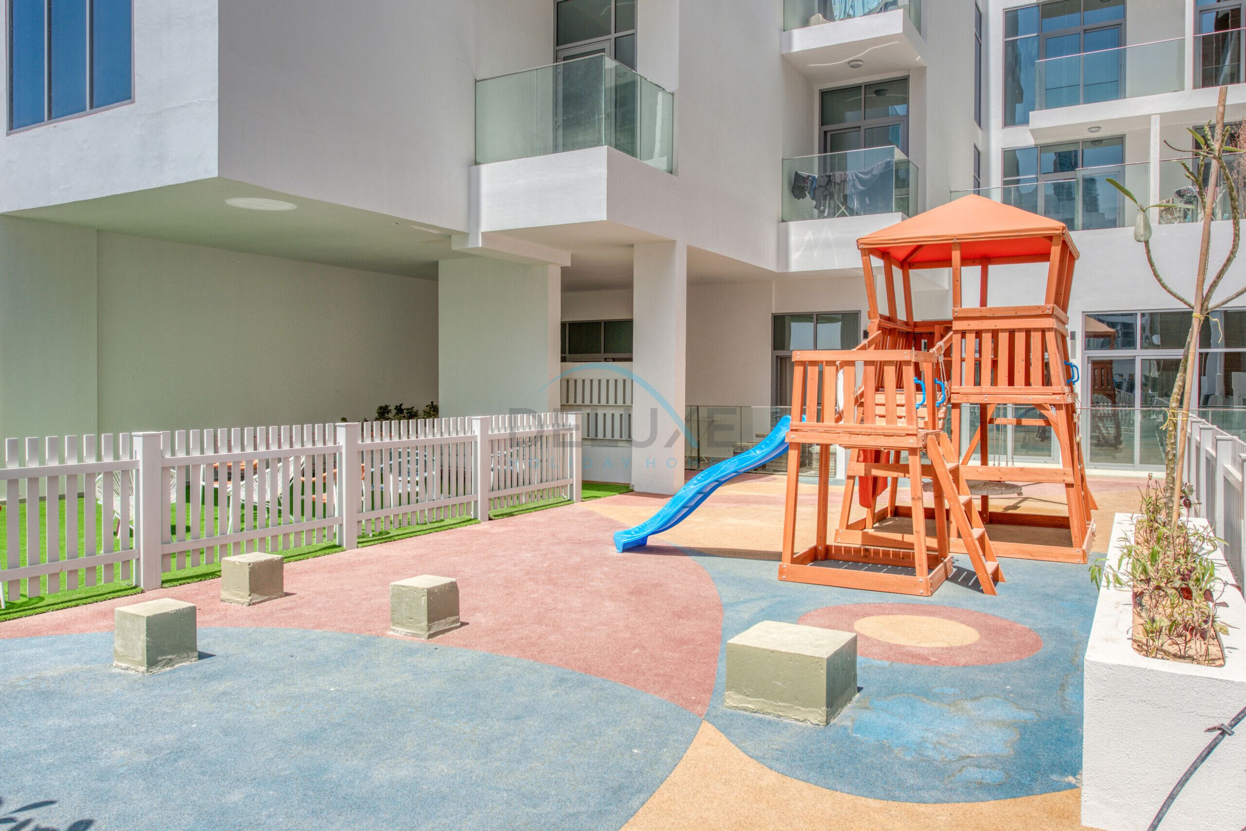 Un espace de jeux pour enfants avec un toboggan, une structure d’escalade en bois et une clôture blanche.
