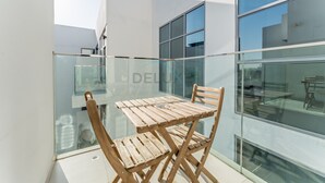 A balcony with a wooden table and chairs, a glass railing, and a view of the interior through large windows. - Balcony Offering Community Views 1BR w/AsstRm,Walking Distance to CommunityPark (Dubai)
