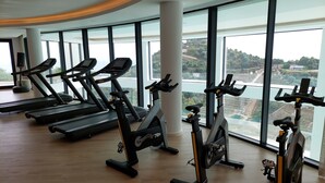 A gym with treadmills, stationary bikes, and a large window with a view of a hilly landscape.