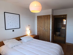 Quarto com cama, quadro emoldurado, guarda-roupa de madeira e banheiro visível por uma porta aberta.
