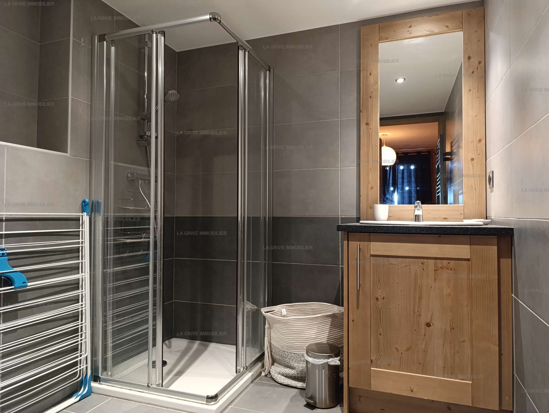 A modern bathroom with a glass shower enclosure, a wooden vanity, and a mirror above the sink.