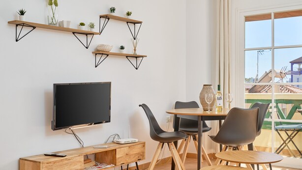 Ein modernes Wohnzimmer mit Flachbildfernseher, Holzregalen und einem Essbereich mit Stühlen und einem Tisch.