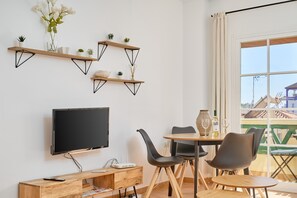 Una sala de estar moderna con televisor de pantalla plana, estanterías de madera y un comedor con sillas y una mesa.