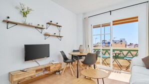 Ein modernes Wohnzimmer mit Flachbildfernseher, Holzböden, einem Esstisch mit Stühlen und einem Balkon mit Blick.