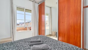 Ein Schlafzimmer mit Bett, einem Vorhangfenster, einer Holztür und Blick auf Gebäude.