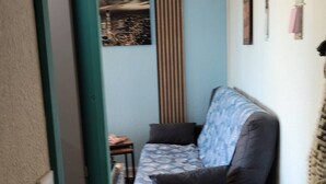 Un couloir étroit avec un canapé et une petite table, un tableau accroché au mur et une porte sur la gauche.