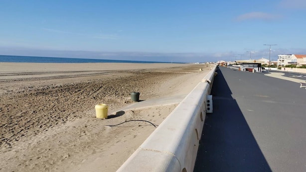 Une route côtière, avec une plage de sable d’un côté et des bâtiments de l’autre.