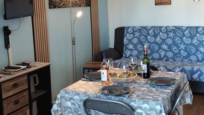 Un coin repas avec une table dressée pour deux personnes, un téléviseur et une horloge murale.