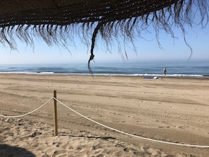 A beach with a rope barrier, a wooden post, and a person walking.