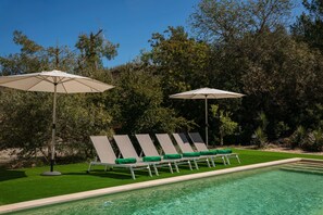 A poolside area with lounge chairs and umbrellas, surrounded by greenery. - Villa Can Bassetes (Ibiza)