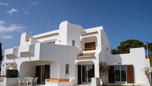Eine moderne, weiße Villa mit Terrasse, Sitzgelegenheiten im Freien und Blick auf die umliegende Landschaft.
